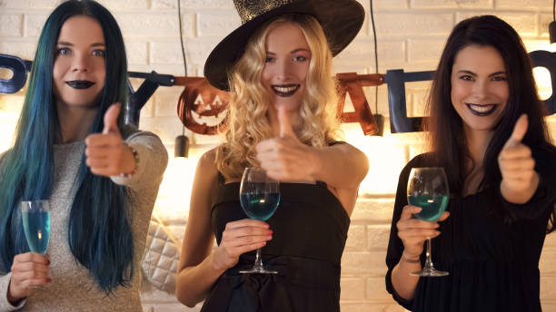 três mulheres bonitas que mostram os polegares acima do gesto, tendo o divertimento na véspera de halloween - witchcraft heights - fotografias e filmes do acervo