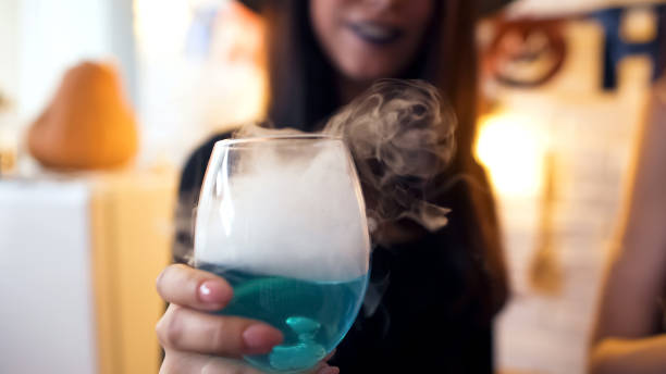 witch showing blue cocktail with white smoke at halloween party, having fun - witchcraft heights imagens e fotografias de stock