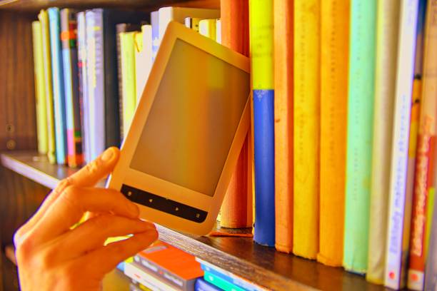 istock Electronic book picked from a library shelf. The electronic book on a bookshelf among the many books in the library. Books and library concept 1131894317