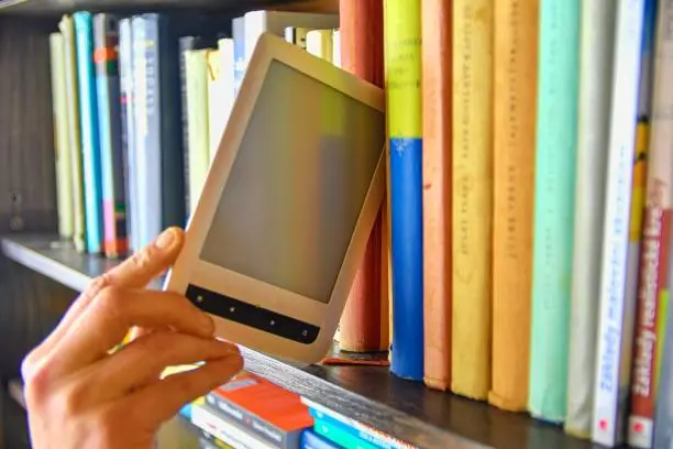 Photo of Electronic book picked from a library shelf. The electronic book on a bookshelf among the many books in the library. Books and library concept