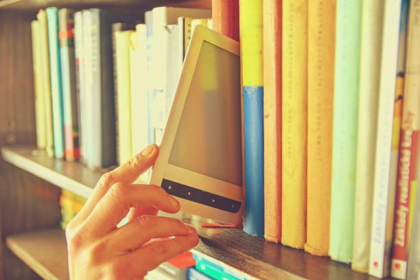 istock Electronic book picked from a library shelf. The electronic book on a bookshelf among the many books in the library 1131894328