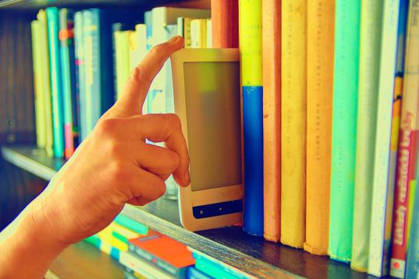 istock Electronic book picked from a library shelf. The electronic book on a bookshelf among the many books in the library. Books and library concept 1131894330