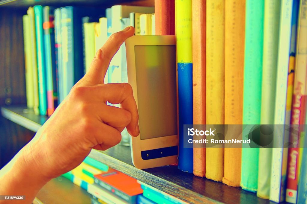 Electronic book picked from a library shelf. The electronic book on a bookshelf among the many books in the library. Books and library concept Electronic book picked from a library shelf. The electronic book on a bookshelf among the many books in the library. Books and library concept. Advice Stock Photo