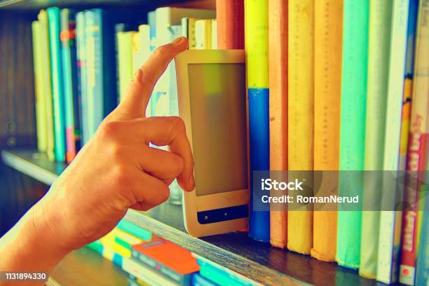 Electronic Book Picked From A Library Shelf The Electronic Book On A Bookshelf Among The Many Books In The Library Books And Library Concept Stock Photo - Download Image Now