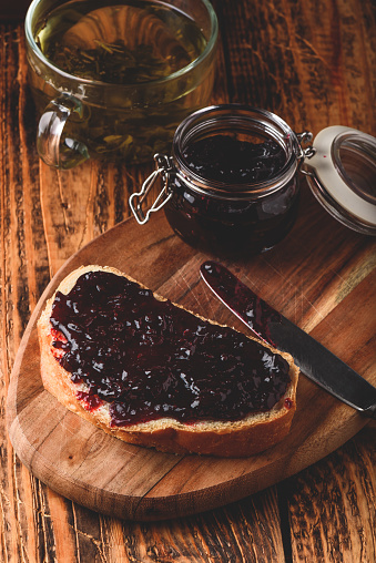 Toast with berry jam on cutting board and cup of green tea in rustic setting