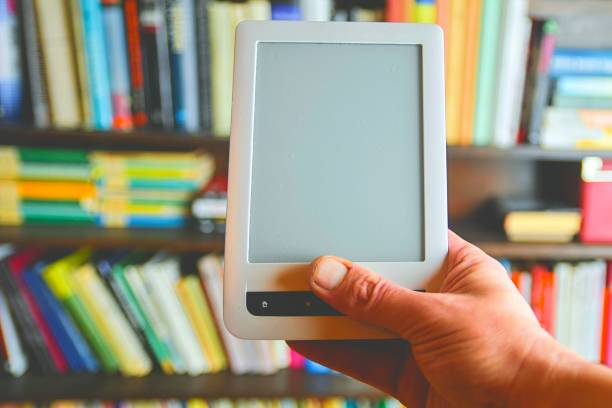 istock E-book or digital reading tablet device. E-book in man's hand.  On the background is the shelf with bright real books. Online shopping books concept 1131898128