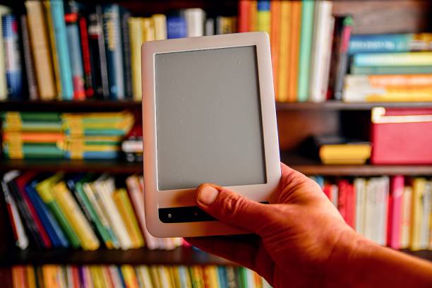 istock E-book or digital reading tablet device. E-book in man's hand.  On the background is the shelf with bright real books. Online shopping books concept 1131898133