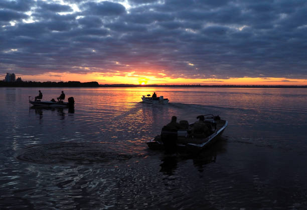 silhueta dos pescadores que dirigem para fora no nascer do sol a seu siteo favorito da pesca - bass - fotografias e filmes do acervo