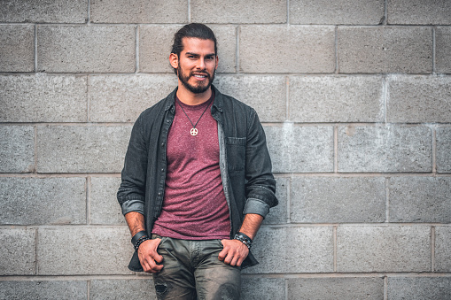 Portrait of confident male hipster. Smiling man is wearing casuals. He is leaning against wall at city.