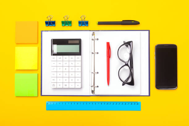 istock Top view of working space table with mobile phone, notebook and pen isolated on yellow background 1131900465