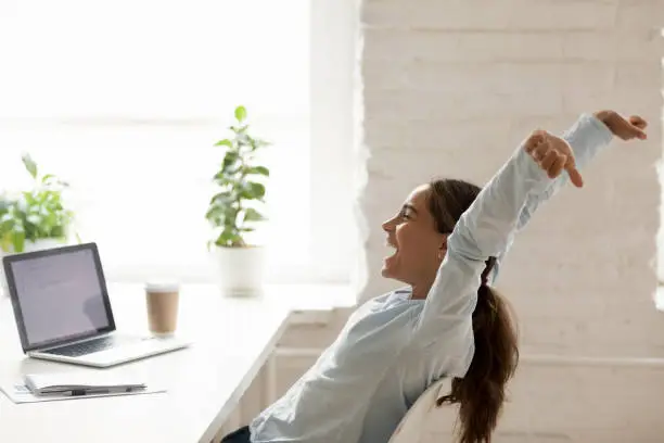 Photo of Cheerful woman stretching raising hands up sitting at workplace
