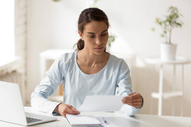 Serious woman sitting at desk reading letter Serious self-employed mixed race businesswoman holding document received letter from service company about payment details or changes, students reading notification about scholarship refusal concept charging sports photos stock pictures, royalty-free photos & images