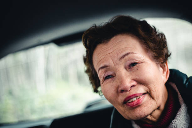 Happy elderly Asian woman lying in bed and peacefully looking out the window at home.