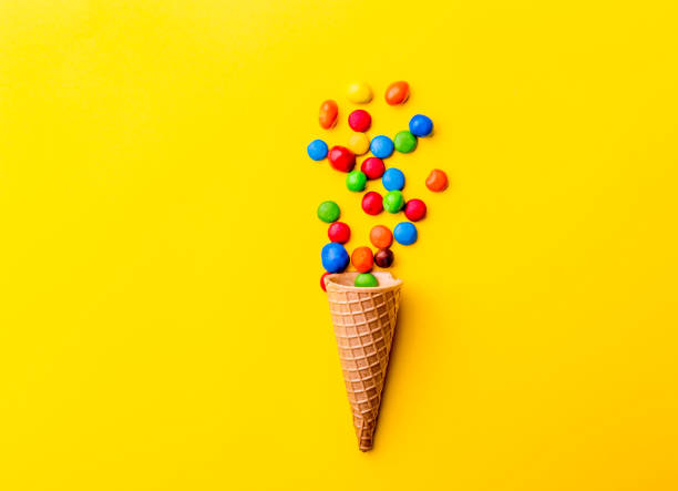 Ice creame cone with candy on yellow background. Minimalistic concept