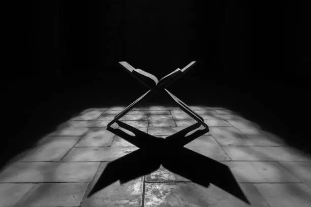 Quran on wooden stand , open in the mosque for prayers with strong shadow in the ground , black and white