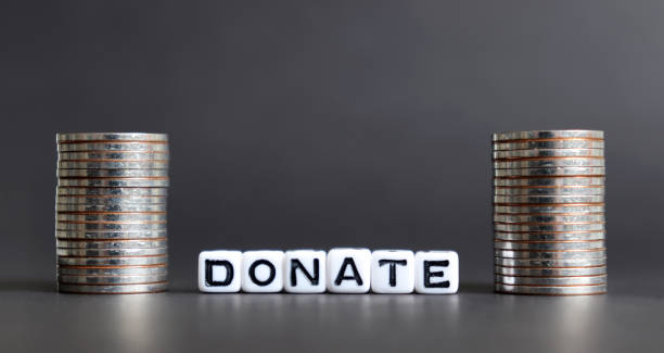 istock Alphabet cube with DONATE letters on black background. Cube and two stack of coins. 1131931617