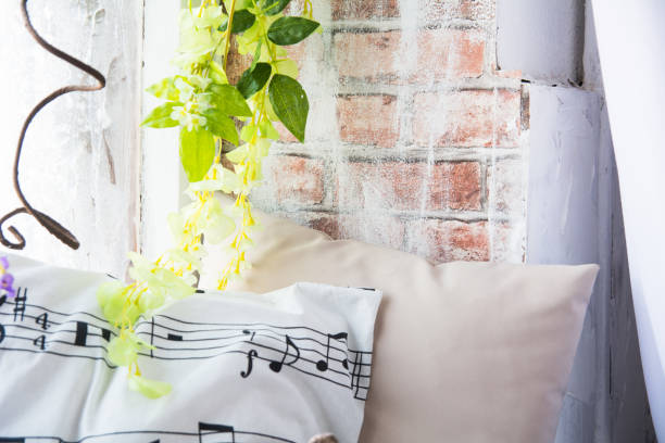 istock Pillow with musical notes on the windowsill with flowers. Brick wall background with artificial flowers 1131940744