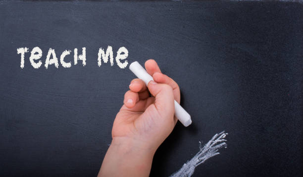 istock Hand with  white chalk and black board with teach me label 1131941838