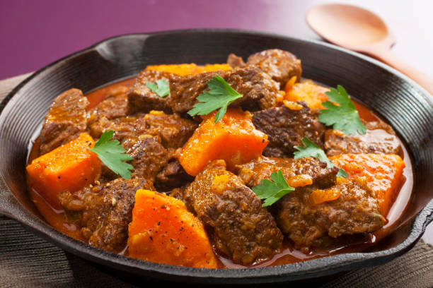 Tagine or Stew with Sweet Potato Chunks and Cilantro Garnish Moroccan tagine or stew of beef with sweet potato, in a cast iron pan. tajine stock pictures, royalty-free photos & images