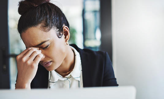 Shot of a young businesswoman looking stressed while working at her desk in a modern office