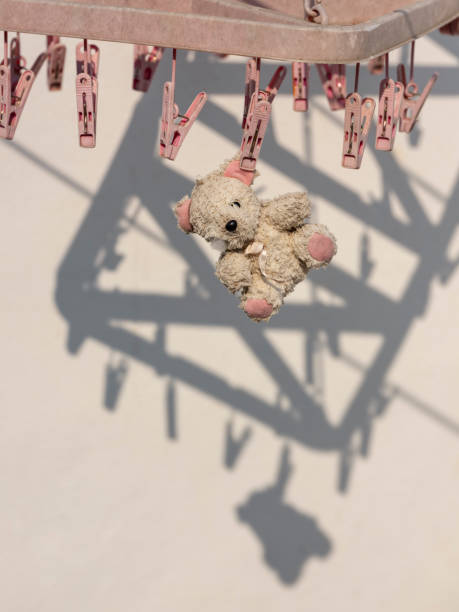 Old small worn out and broken children's toy teddy bear with one eye missing hanging out to dry in the sun on a clothes peg on a plastic drying rack, concept image relating to worn out, nothing last forever, material, reusable, recycling, humble, saving, poverty etc. viejo pequeño desgastado y roto oso de peluche de juguete de los niños con un ojo que falta colgando para secar en el sol en una clavija de ropa en un estante de secado de plástico, imagen conceptual relacionada con desgastado, nada dura para siempre, p