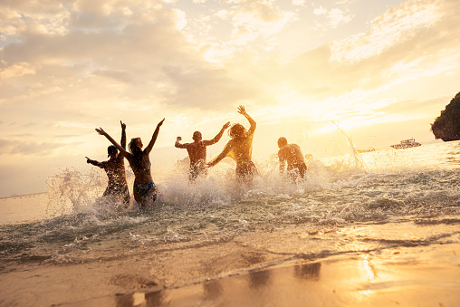Happy friends runs or having fun at idyllic sunset sea