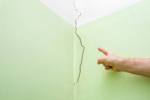 Man's hand finger pointing to cracked corner wall in house. Building problems and solutions concept. Man's hand finger pointing to cracked corner wall in house. Building problems and solutions concept. defection stock pictures, royalty-free photos & images