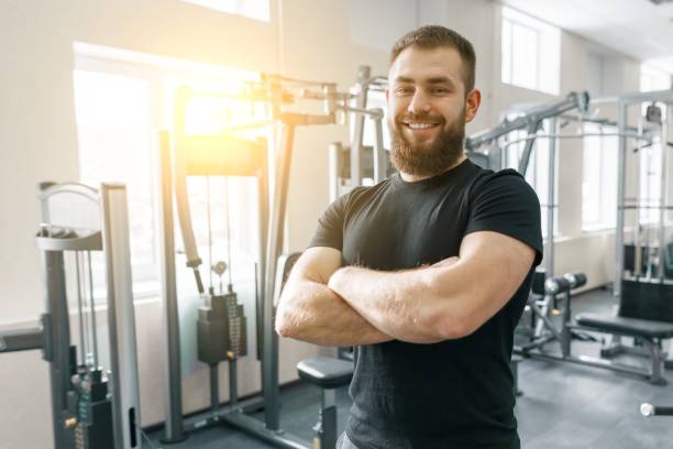 portrait of smiling personal fitness trainer in gym, confident man with folded hands looking at camera. fitness, sport, training, people concept - secrecy instructor exercising individuality imagens e fotografias de stock