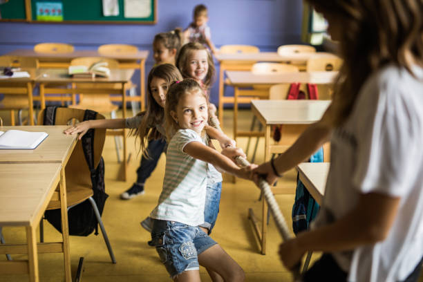 istock Playful elementary students playing tug-of-war with their teacher in the classroom. 1131968483