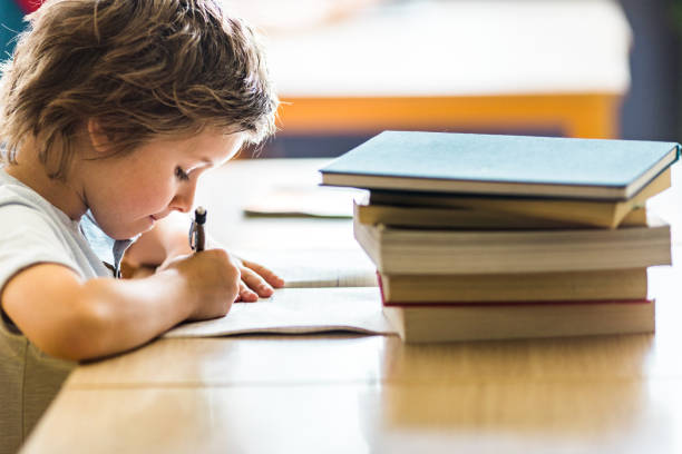 istock Profile view of schoolboy writing on a class at school. 1131969306