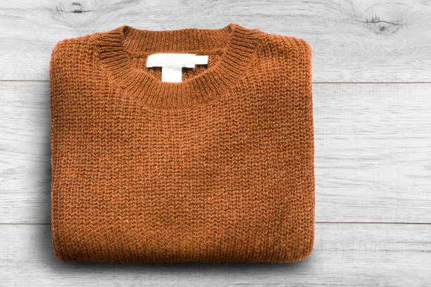 Folded brown knitted sweater on white wooden background