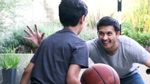 Hispanic father and son playing basketball together outdoors