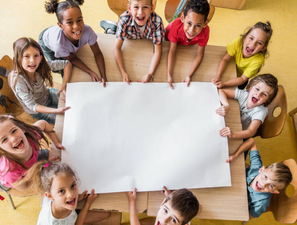 powyżej widok szczęśliwych uczniów szkół podstawowych z pustym papierem w klasie. - caucasian white poster little boys zdjęcia i obrazy z banku zdjęć