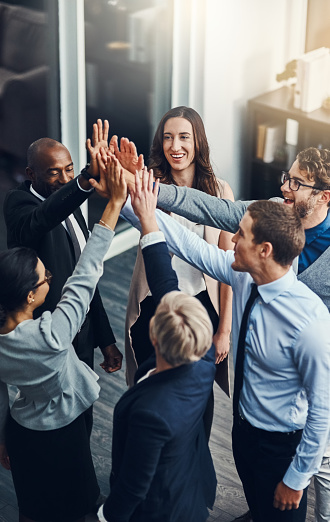 High angle shot of a group of businesspeople high fiving in an office