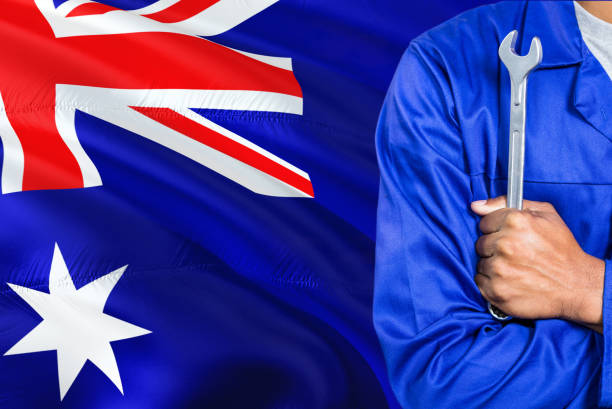 o mecânico australiano no uniforme azul está prendendo a chave de encontro ao fundo de ondulação da bandeira de austrália. técnico de armas cruzados. - ozzie - fotografias e filmes do acervo