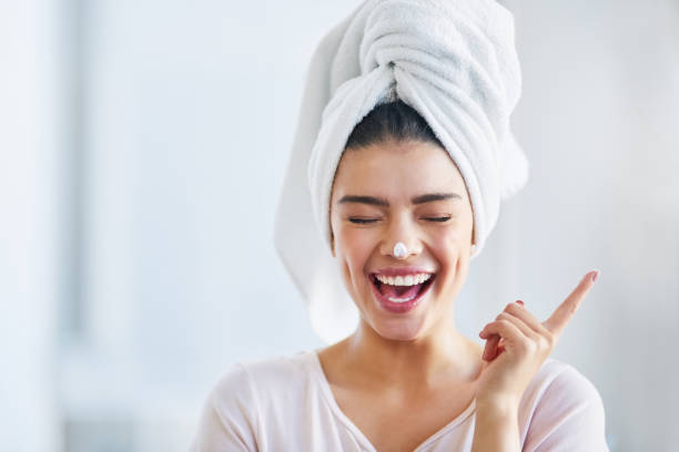 Glowing skin automatically makes me happy Shot of a beautiful young woman applying moisturizer to her skin in the bathroom at home woman wrapped in bath towel stock pictures, royalty-free photos & images