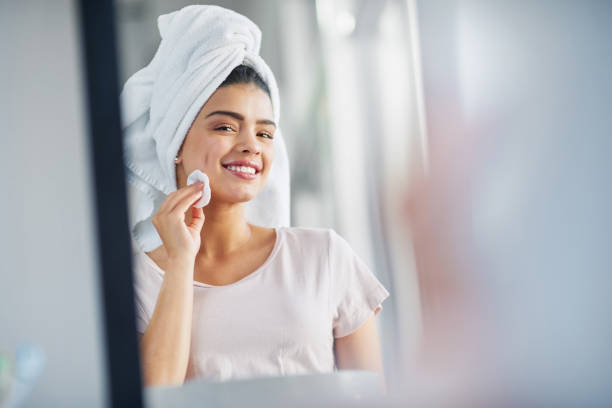 Cleansing her skin to reveal her natural beauty Shot of a beautiful young woman cleaning her face with cotton wool in the bathroom at home woman wrapped in bath towel stock pictures, royalty-free photos & images