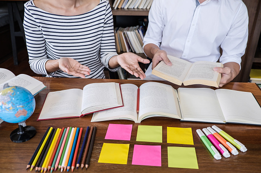 High school or college student group sitting at desk in library studying and reading, doing homework and lesson practice preparing exam to entrance, education concept.