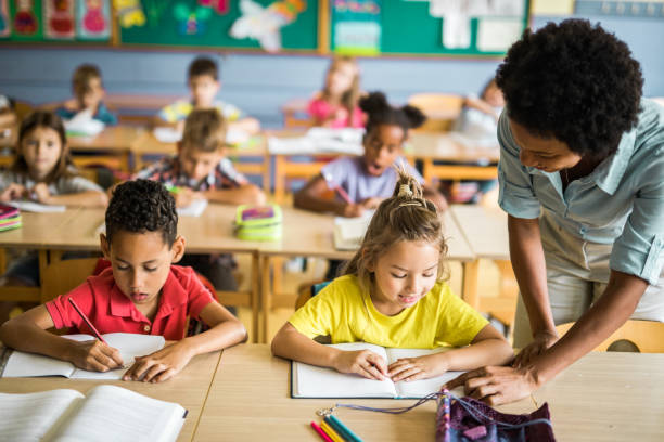 istock Happy black teacher assisting elementary kids on a class at school. 1131977956