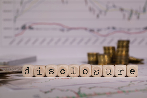 Word DISCLOSURE composed of wooden letters. Stacks of coins in the background. Closeup