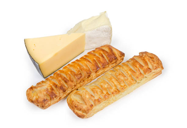 Two baked sticks made of flaky pastry and filled with cheese, pieces of hard and soft cheese on a white background