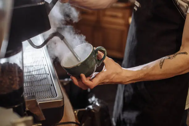 young male barista using coffeemaker to prepare super coffee