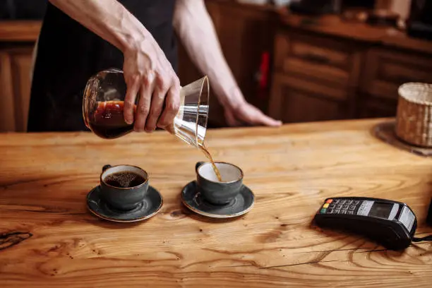 man's hands holding glass coffeemaker and pouring coffee