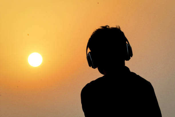 silhouette de l'homme avec le casque sur le fond de ciel de coucher du soleil. silhouette d'homme heureux écoutant la musique. - romantic sky audio photos et images de collection