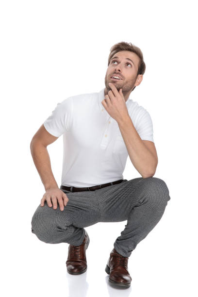 smiling crouched casual man looks up and thinks smiling crouched casual man looks up and wonders what is it over there on white background bending stock pictures, royalty-free photos & images