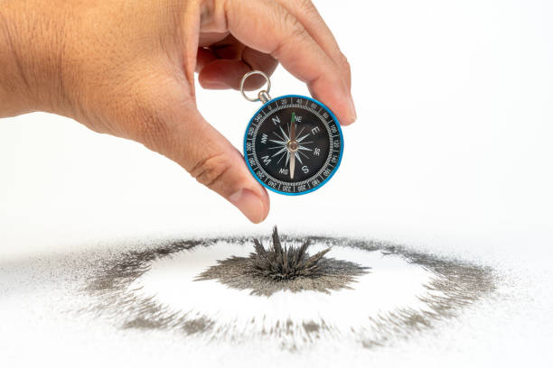 istock Hand holding classic compass over iron powder magnetic field on white background. Scientific experiment in science class in school. 1131989435
