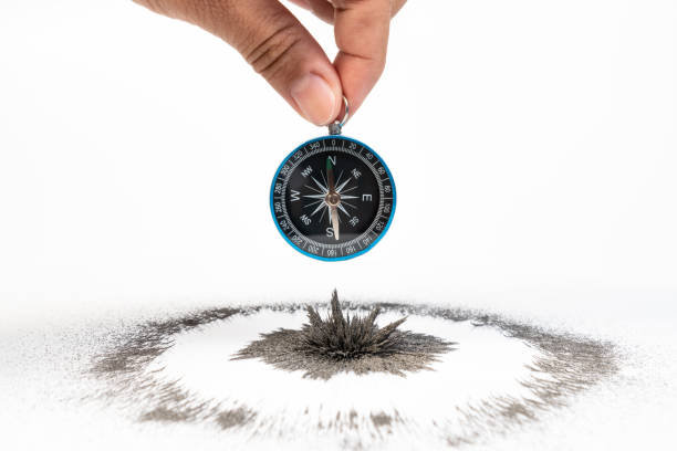 istock Hand holding classic compass over iron powder magnetic field on white background. Scientific experiment in science class in school. 1131989438