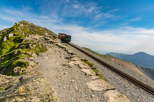 Near Llanberis, Gwynedd, Wales, UK - June 14, 2017: View from the Llanberis Path, with a train of the Snowdon Mountain Railway on the way to Mount Snowdon, and people sitting in the train