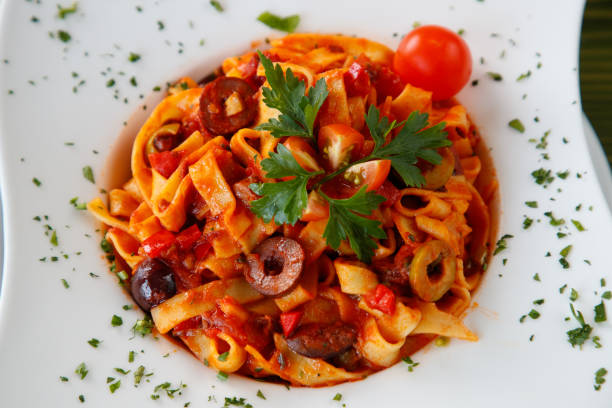 Fettuccine in bolognese sauce served with olives and fresh tomato, decorated with parsley
