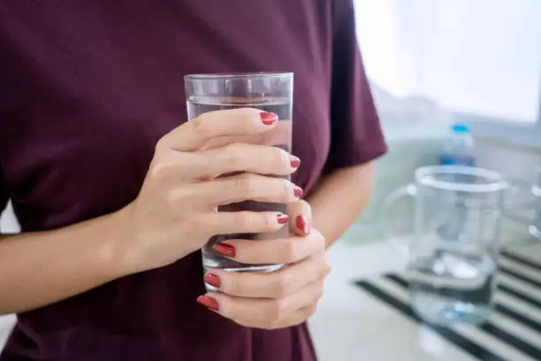 Close up of unknown woman hands holding a glass of fresh water in the kitchen